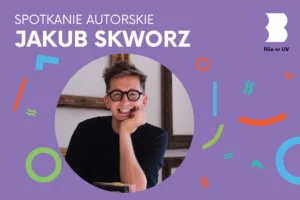 Młody mężczyzna w okularach podpierając podbródek ręką uśmiecha się od ucha do ucha.